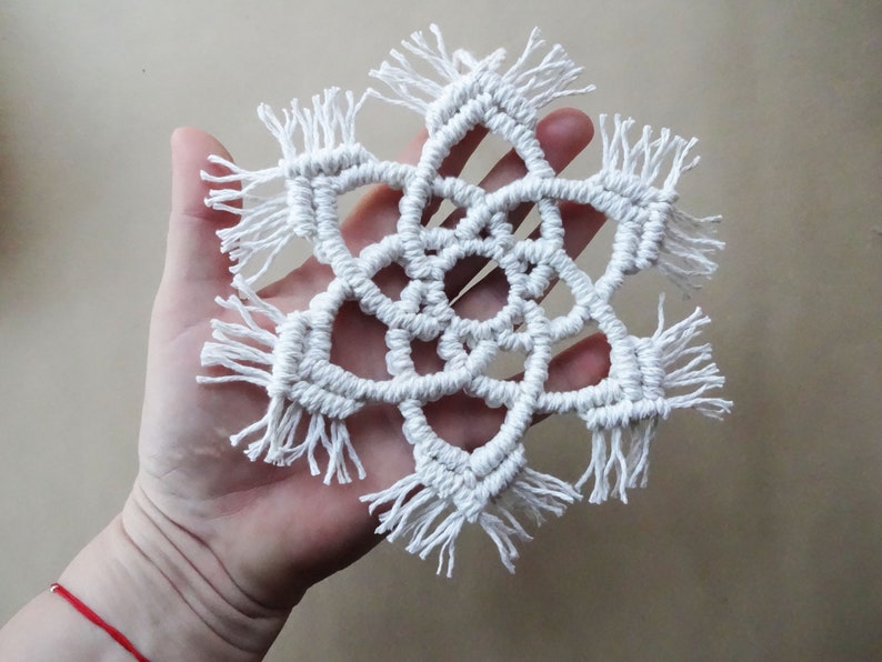May include: White macrame snowflake with fringe details.