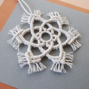 May include: A white macrame snowflake ornament with a fringe border.