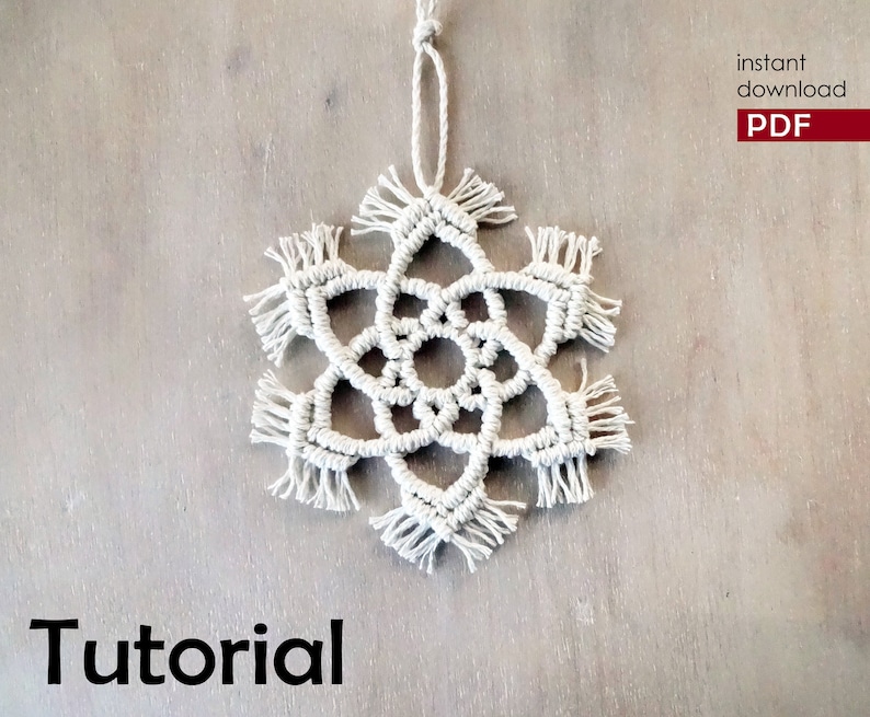 May include: A white macrame snowflake ornament with a fringe border. The ornament is hanging from a white string. The background is a light brown wood surface. The text "Tutorial" is printed in black at the bottom of the image. The text "instant download PDF" is printed in red at the top right of the image.