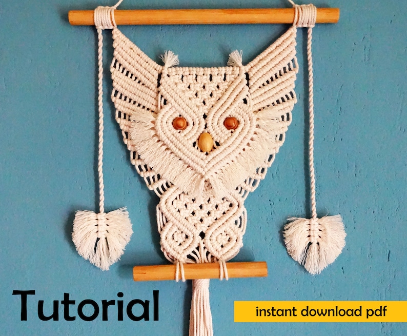 Peut inclure: Une suspension murale en macram&eacute; en forme de hibou blanche avec des chevilles en bois et des glands. Le hibou a des yeux en perles de bois. Le texte "Tutoriel" et "t&eacute;l&eacute;chargement instantan&eacute; pdf" est visible sous le hibou.
