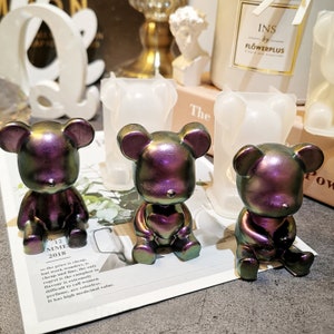 May include: Three iridescent purple and green resin bear figurines sitting in clear silicone molds. The molds are shaped like bears sitting with their paws in front of them. The bears are about 3 inches tall.