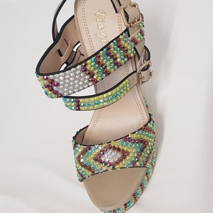 May include: Beige platform sandals with multiple straps adorned with colorful rhinestones. The sandals have a buckle closure and a platform sole. The brand name "Via gemini" is visible on the insole. The sandals are designed for a fashionable look.