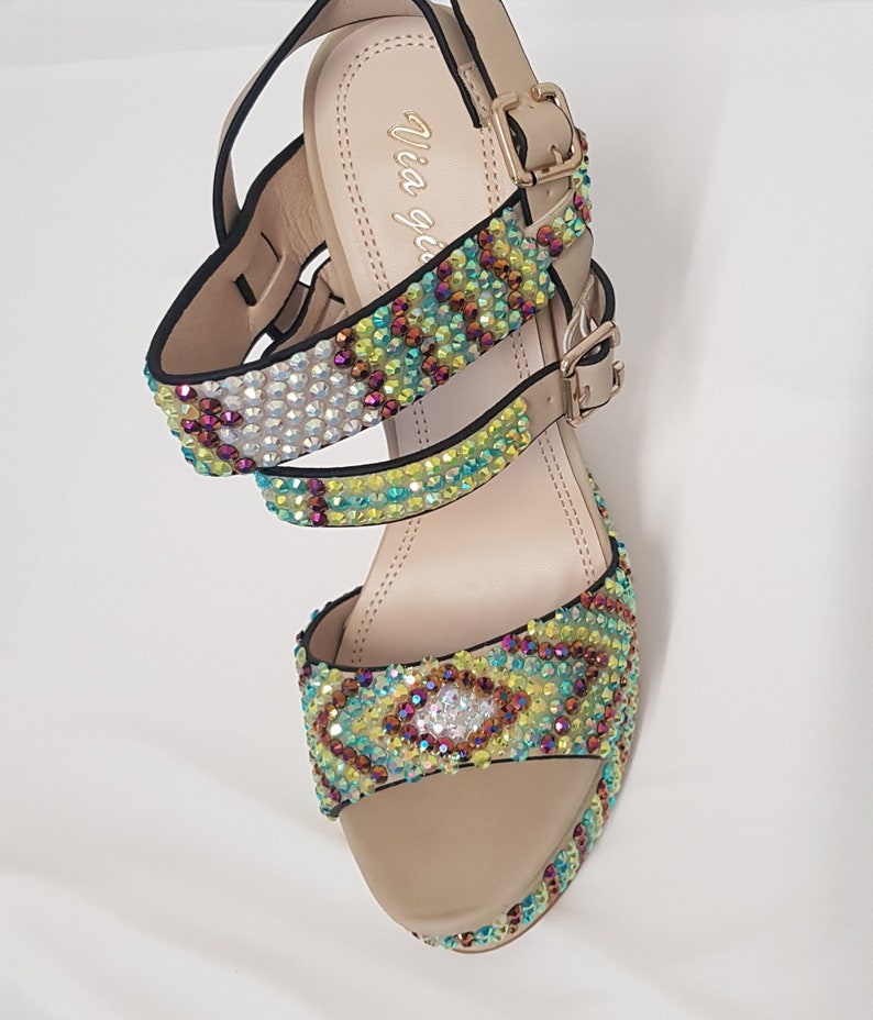 May include: Beige platform sandals with multiple straps adorned with colorful rhinestones. The sandals have a buckle closure and a platform sole. The brand name "Via gemini" is visible on the insole. The sandals are designed for a fashionable look.