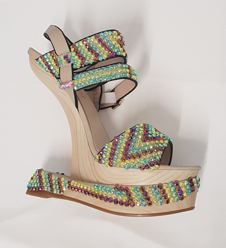 May include: A platform sandal with a wooden wedge heel. The beige straps and platform are adorned with colorful iridescent rhinestones. The heel is approximately 5 inches high.