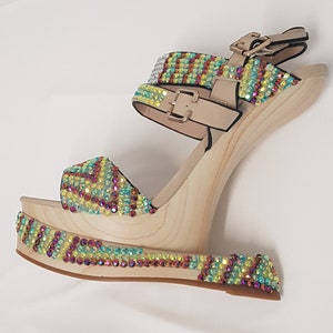 May include: A single platform sandal with a wooden wedge heel. The sandal features a beige ankle strap and toe strap, both adorned with iridescent rhinestones in a colorful pattern. The wooden platform and heel are light-colored.