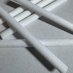 May include: A close-up shot of several white foam rods, arranged in a scattered pattern. The rods are cylindrical and have a slightly textured surface. The background is a light gray color.