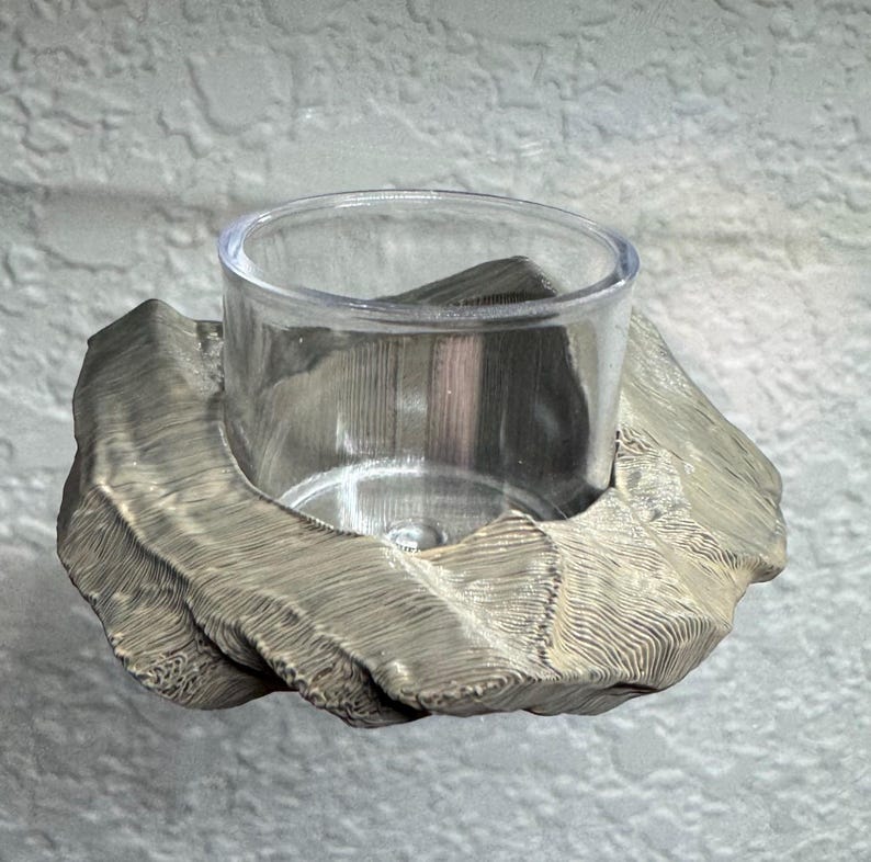 May include: A silver-colored votive candle holder with a clear glass cup. The holder has a textured, organic design. The candle holder is designed to hold a small tea light candle.
