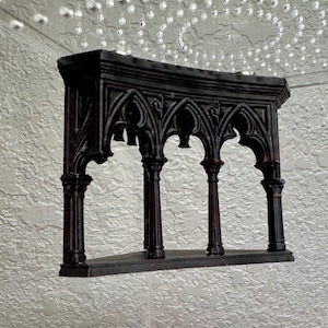 May include: A black, gothic-style shelf with arched openings and decorative columns. The shelf is made of a dark material and has a textured surface. The design is reminiscent of medieval architecture.
