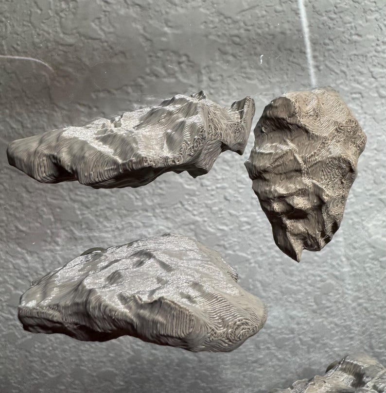 May include: Three gray, textured, rock-like sculptures are suspended in the air. The sculptures have a rough, layered appearance, with visible ridges and patterns. The lighting creates highlights and shadows, emphasizing the three-dimensional forms.