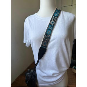 May include: A camera strap with a black base and a colorful floral pattern in shades of blue, gold, and white.