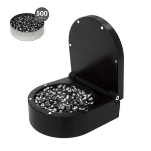 Puede incluir: Un contenedor negro con bisagras lleno de perdigones plateados, con una lata separada de perdigones en la esquina superior izquierda. La lata está etiquetada como "500 perdigones". El contenedor está diseñado para contener y dispensar perdigones.