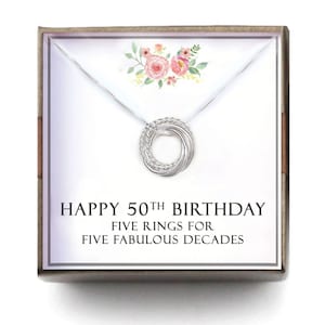 May include: A silver necklace with a circle pendant made of five intertwined rings. The necklace is in a white box with the text "Happy 50th Birthday Five Rings for Five Fabulous Decades".