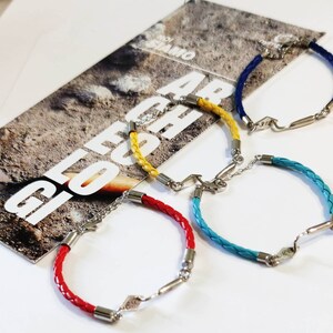 May include: Four braided leather bracelets with silver clasps and metal accents. The bracelets are red, yellow, blue, and turquoise.