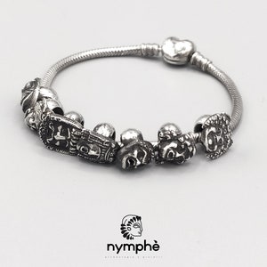 Peut inclure: Un bracelet à breloques en argent avec un charme en forme de cœur et plusieurs breloques aux motifs différents. Les breloques sont toutes en argent et présentent un design détaillé et complexe.