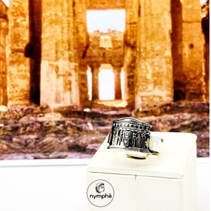 Peut inclure: Bague en argent avec un design 3D détaillé d'un temple grec antique. La bague est présentée sur une boîte blanche avec le mot "nymphé" imprimé dessus.