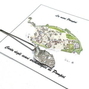 Op de afbeelding: Een zilveren ketting met een hanger in de vorm van een kaart van Pompeii. De hanger is gedetailleerd met de lay-out van de oude stad. De ketting wordt getoond op een witte kaart met de tekst "La mini Pompei" en "Carta degli scavi archeologici di Pompei".