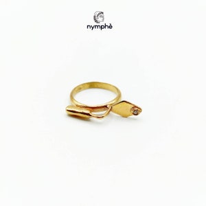 May include: A gold ring with a trowel design and a small diamond set in the trowel. The ring is made by the company "nymph&eacute;".