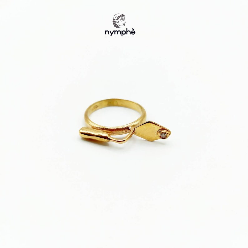 May include: A gold ring with a trowel design and a small diamond set in the trowel. The ring is made by the company "nymph&eacute;".