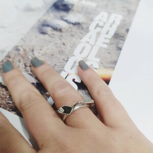 May include: A silver ring with a black stone set in a unique, abstract design. The ring is worn on a person's finger.