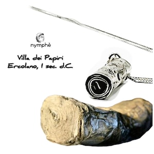 Op de afbeelding: Een zilverkleurige hangerketting met een cilindrische bedel. De bedel heeft een getextureerd oppervlak en een donker interieur. De afbeelding bevat ook een stuk hout en de tekst "Villa dei Papiri Ercolano, I sec. d.C."