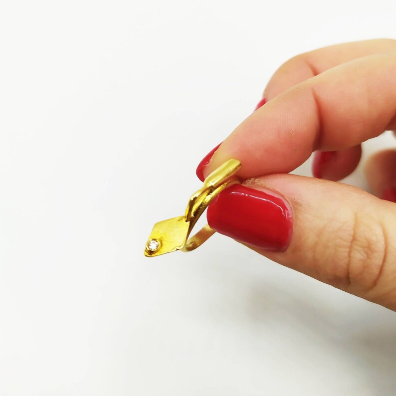 May include: A gold ring with a small diamond set in a square shape. The ring is open and has a simple design.