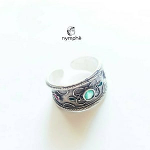 May include: A silver ring with an ornate design and green and red gemstones.