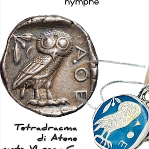 Può includere: Una moneta d'argento e un ciondolo con un disegno di gufo. La moneta, con il testo "Tetradracma di Atene meta VI sec.a.C.", mostra un gufo con un ramo d'ulivo. Il ciondolo ha uno sfondo in smalto blu e un disegno di gufo argentato.