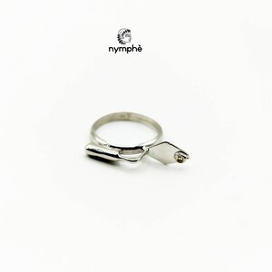 May include: A silver ring with a trowel design. The trowel has a small, clear stone set in the handle.