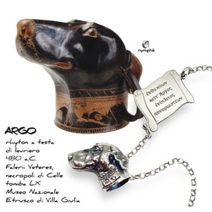 May include: A black and brown ceramic rhyton in the shape of a dog's head, with a silver dog head pendant necklace. The rhyton has a decorative band with figures. The necklace has a scroll pendant with Greek text.
