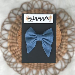 Può includere: Un papillon in denim blu su uno sfondo nero con il testo "milamade" e un nome utente sui social media.