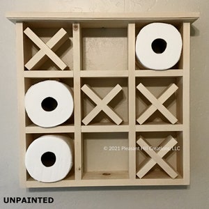 May include: Unpainted wooden tic-tac-toe game with three rolls of white toilet paper. The game board is made of light-colored wood and has a grid of nine squares. The game pieces are wooden X's and O's. The text "UNPAINTED" is at the bottom.