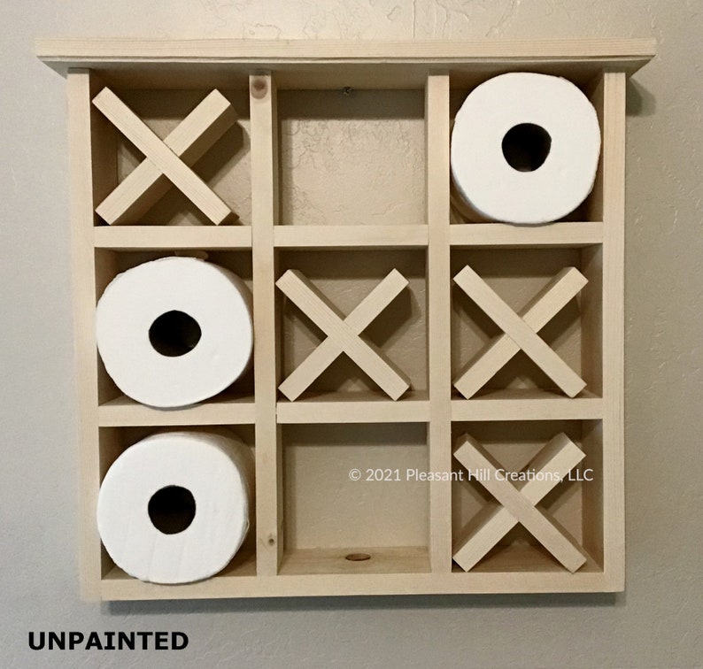 May include: Unpainted wooden tic-tac-toe game with three rolls of white toilet paper. The game board is made of light-colored wood and has a grid of nine squares. The game pieces are wooden X's and O's. The text "UNPAINTED" is at the bottom.