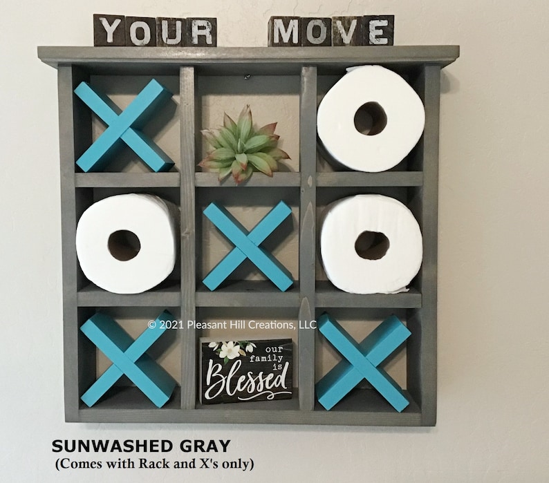 May include: A gray wooden tic-tac-toe game with turquoise X's and spaces for toilet paper rolls. The top has the words "YOUR MOVE" in block letters. A small sign reads "our family is Blessed".