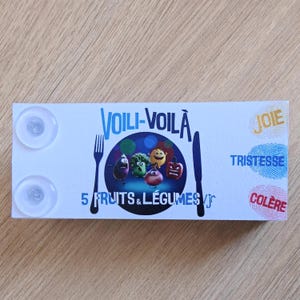 Könnte beinhalten: Eine weiße rechteckige Karte mit dem Text "VOILI-VOILÀ" und "5 FRUITS & LÉGUMES/jr". Die Karte zeigt Illustrationen von anthropomorphen Früchten und Gemüse, eine Gabel und ein Messer. Die Wörter "JOIE", "TRISTESSE" und "COLÈRE" sind ebenfalls vorhanden.