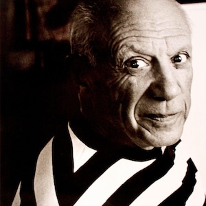 Op de afbeelding: Zwart-wit portret van Pablo Picasso, gekleed in een gestreept shirt. Het Apple-logo en de slogan "Think different" zijn zichtbaar. Een vintage advertentie.