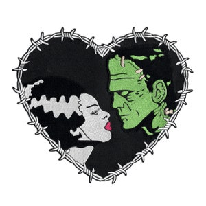 May include: A black heart-shaped patch with a barbed wire border. The patch features a green Frankenstein's monster and a grey Bride of Frankenstein. The two figures are looking at each other.
