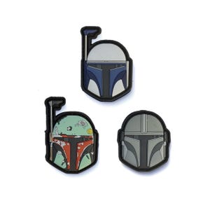Può includere: Tre toppe a forma di casco con bordi neri. Uno è blu e bianco, un altro rosso, verde e arancione, e il terzo grigio. Le toppe sono probabilmente per abbigliamento o accessori.
