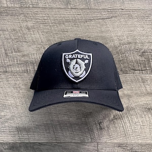 Pode incluir: Boné de caminhoneiro preto com um remendo preto e branco que diz "GRATEFUL" e apresenta uma cabeça de urso com uma guitarra atrás.