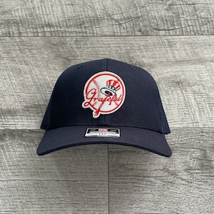 May include: A navy blue baseball cap with a white mesh back. The front of the cap features a red, white and blue embroidered patch with a baseball, a baseball bat, and the word "Grateful" in a cursive font.