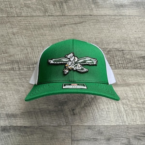 Könnte beinhalten: Grün-weiße Trucker-Mütze mit einem Bären-Motiv im Flug. Die Vorderseite ist grün, die Netzrückseite weiß. Die Mütze hat einen gebogenen Schirm und einen Aufnäher mit einem Bären-Design. Ein Etikett ist auf dem Schirm sichtbar.