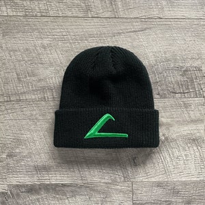 Puede incluir: Gorro de punto negro con un logotipo de triángulo bordado en verde.