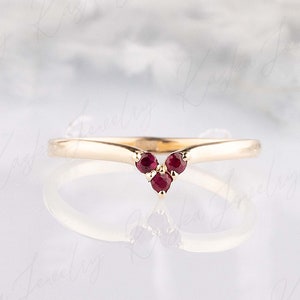 May include: A gold band ring with three small ruby red stones set in a V shape.