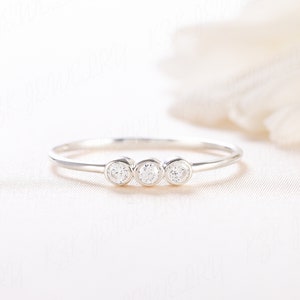 Op de afbeelding: Een delicate zilveren ring met drie kleine ronde diamanten in een rij.