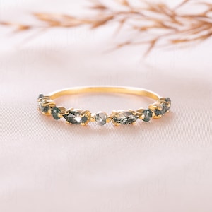 Op de afbeelding: Een delicate gouden ring met een rij marquise-vormige edelstenen. De edelstenen zijn een mix van helder en donkergrijs.