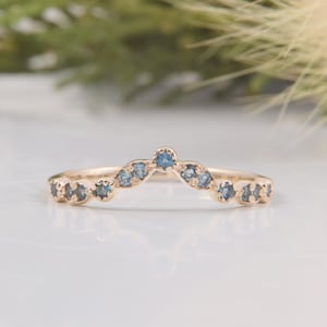 Może przedstawiać: Delikatny złoty pasek z zakrzywionym rzędem małych niebieskich kamieni szlachetnych. Pasek jest zaprojektowany do noszenia jako obrączka ślubna lub pierścionek do układania w stosy.