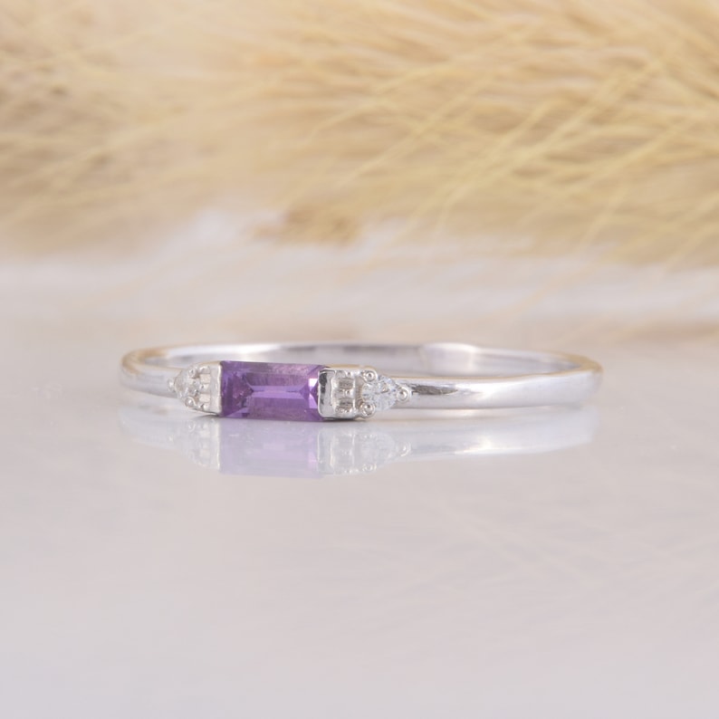 May include: A delicate silver ring with a purple rectangular gemstone and two small diamond accents.