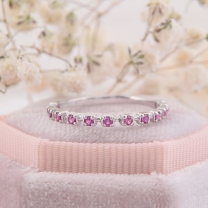 May include: A delicate silver band ring with a row of small pink gemstones.
