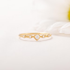 Pode incluir: Um delicado anel de ouro com um pequeno diamante redondo no centro e diamantes menores de cada lado. O anel tem um design de inspira&ccedil;&atilde;o vintage com detalhes intrincados.