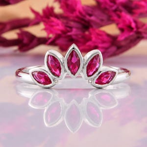 May include: A silver ring featuring five marquise-cut vibrant pink stones arranged in a fan-like arc across the top. The band is smooth and polished, showcasing a symmetrical design with the stones set securely in individual silver bezels.