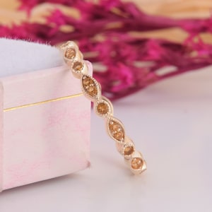 May include: A delicate gold band ring with a row of small, oval-shaped, light brown gemstones.
